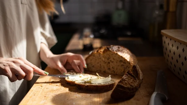 Mujer untando mantequilla sobre una rebanada de pan integral sobre una tabla de cortar de madera