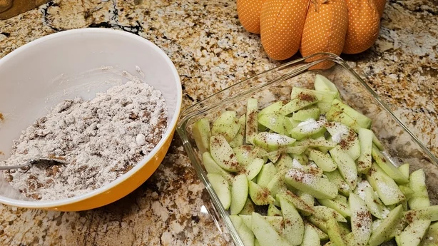 Rebanadas de manzanas Granny Smith junto con harina, nuez moscada y canela en un tazón, preparándose para mezclar los ingredientes para un delicioso postre favorito de temporada.