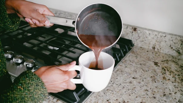 Primer plano de una mujer negra irreconocible vertiendo chocolate caliente en una taza